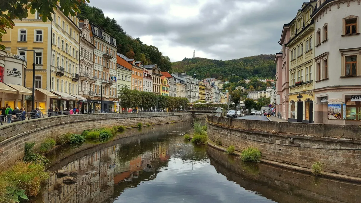 Pastel spa-town buildings lining a river in Karlovy Vary under a cloudy sky Pastel spa-town buildings lining a river in Karlovy Vary under a cloudy sky