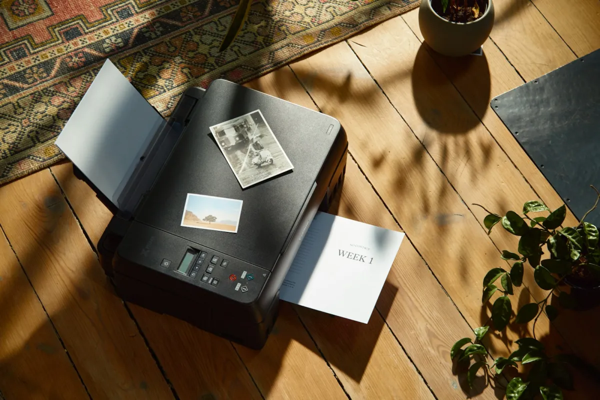 Home printer on a wooden floor with printed photos and a plant