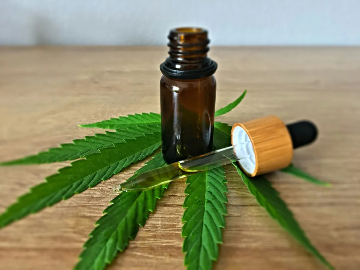 Brown glass dropper bottle of oil on a hemp leaf on a wooden table