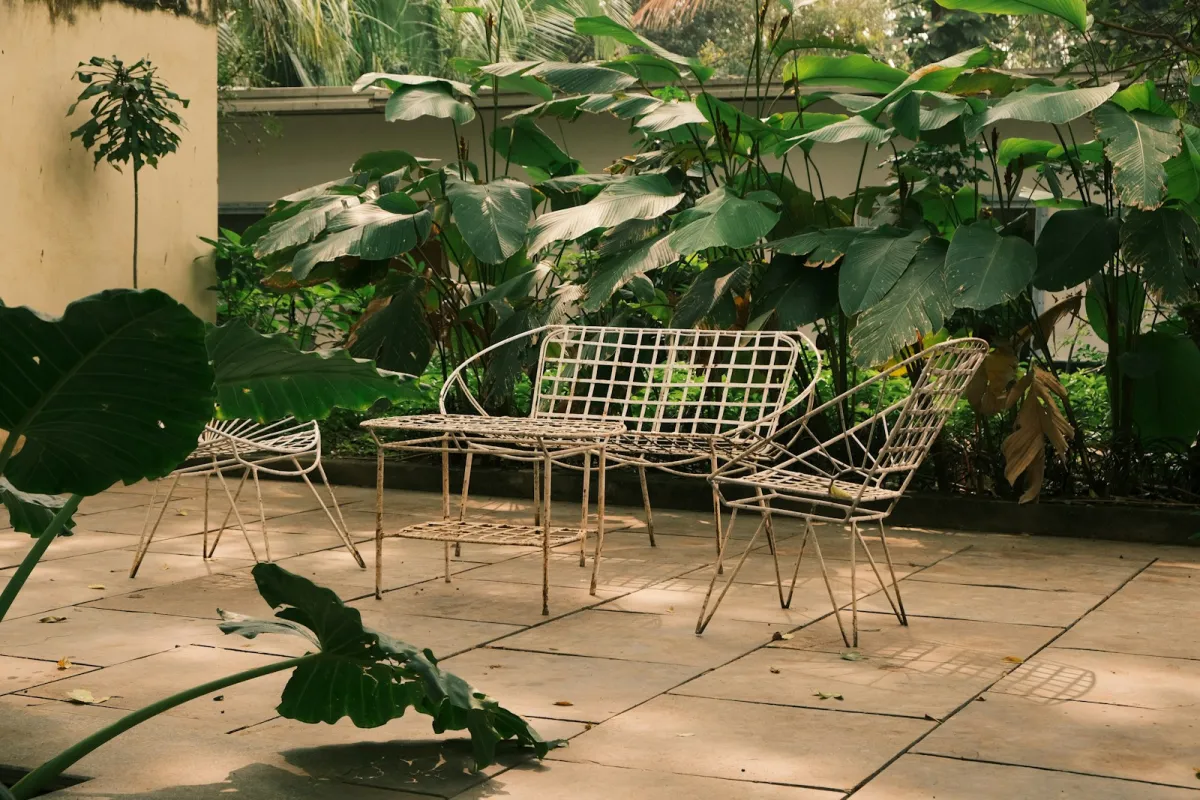 White metal garden furniture set on a paved patio surrounded by leafy plants