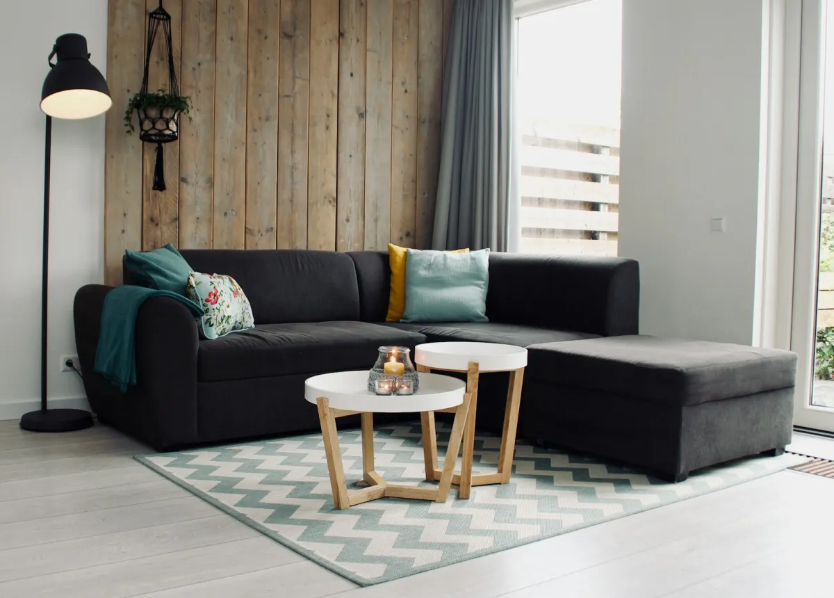 Grey corner sofa with cushions, two round coffee tables and a patterned rug in a bright living room