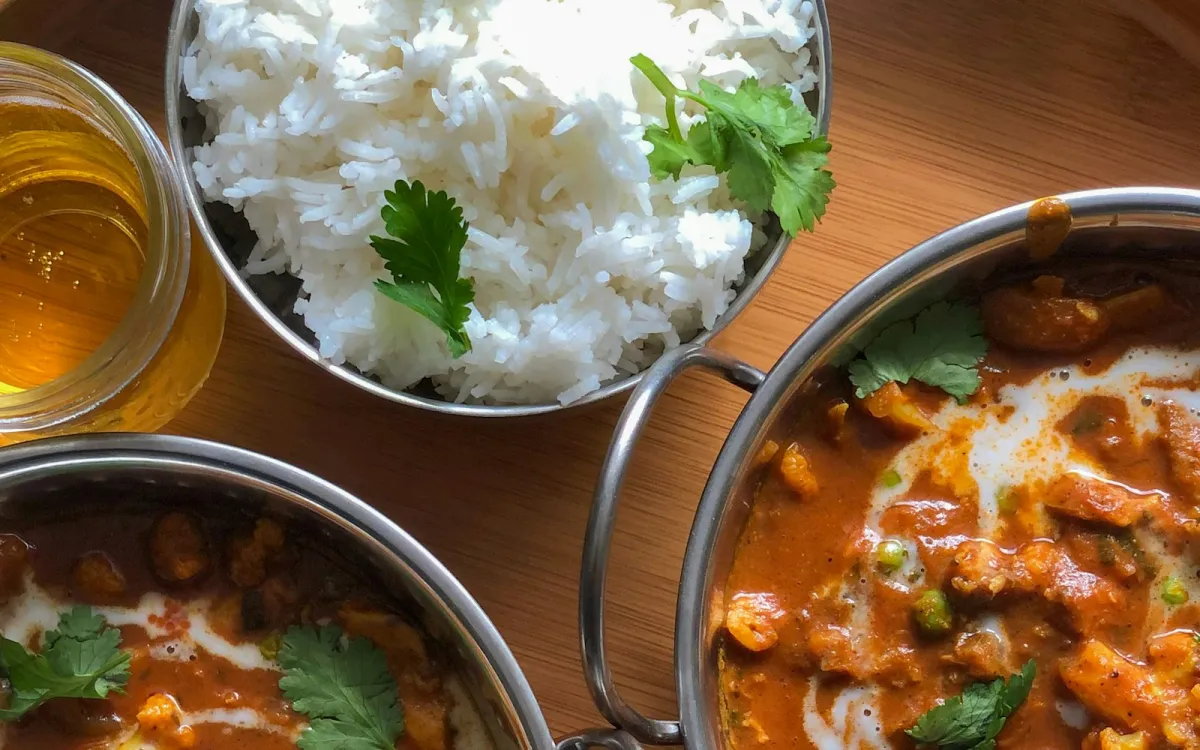 Bowls of curry and basmati rice topped with coriander on a wooden table Bowls of curry and basmati rice topped with coriander on a wooden table