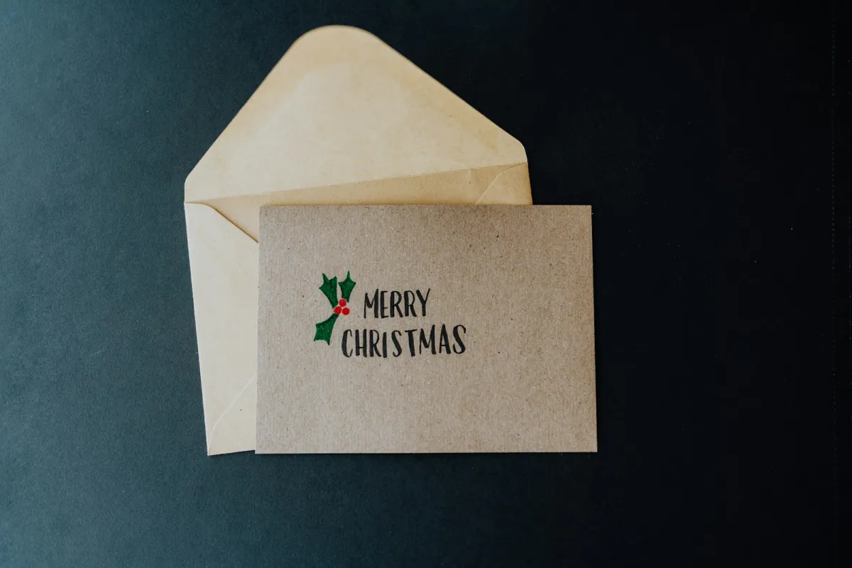 A handwritten Merry Christmas card with holly resting on a kraft paper envelope
