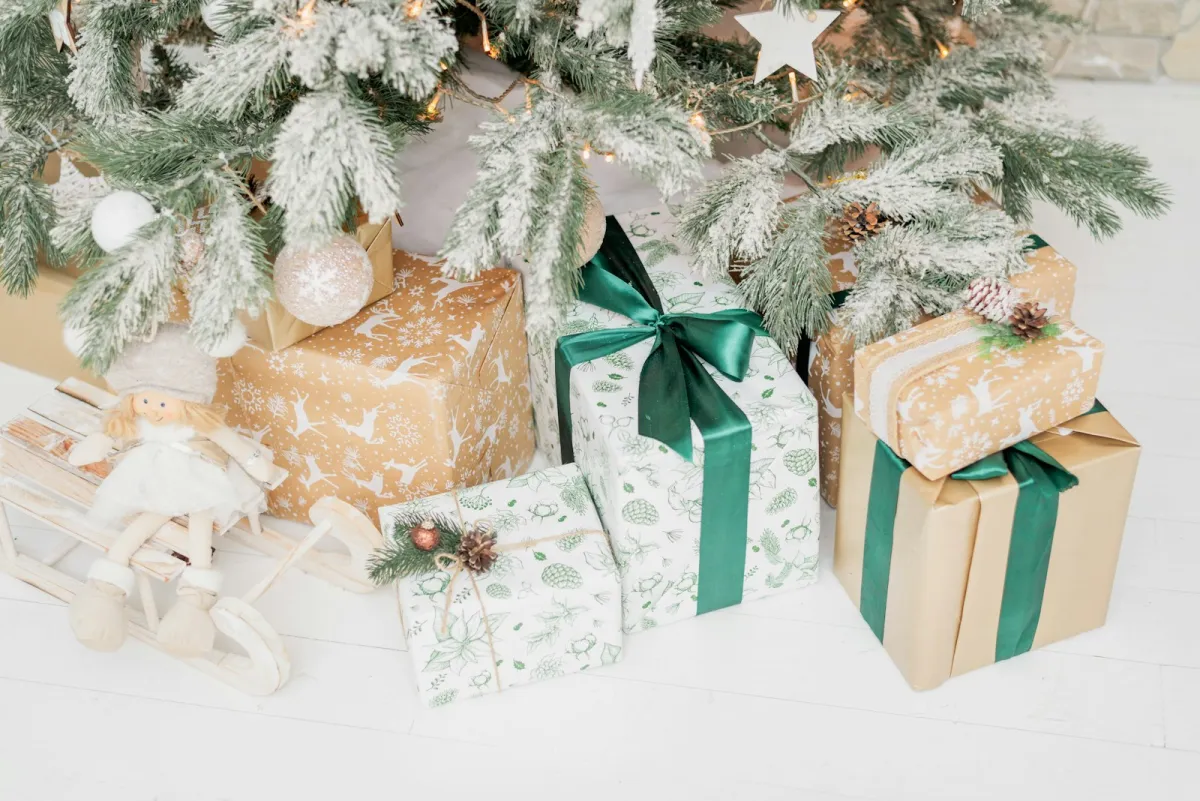 Wrapped Christmas presents and a toy doll on a sledge under a frosted Christmas tree Wrapped Christmas presents and a toy doll on a sledge under a frosted Christmas tree