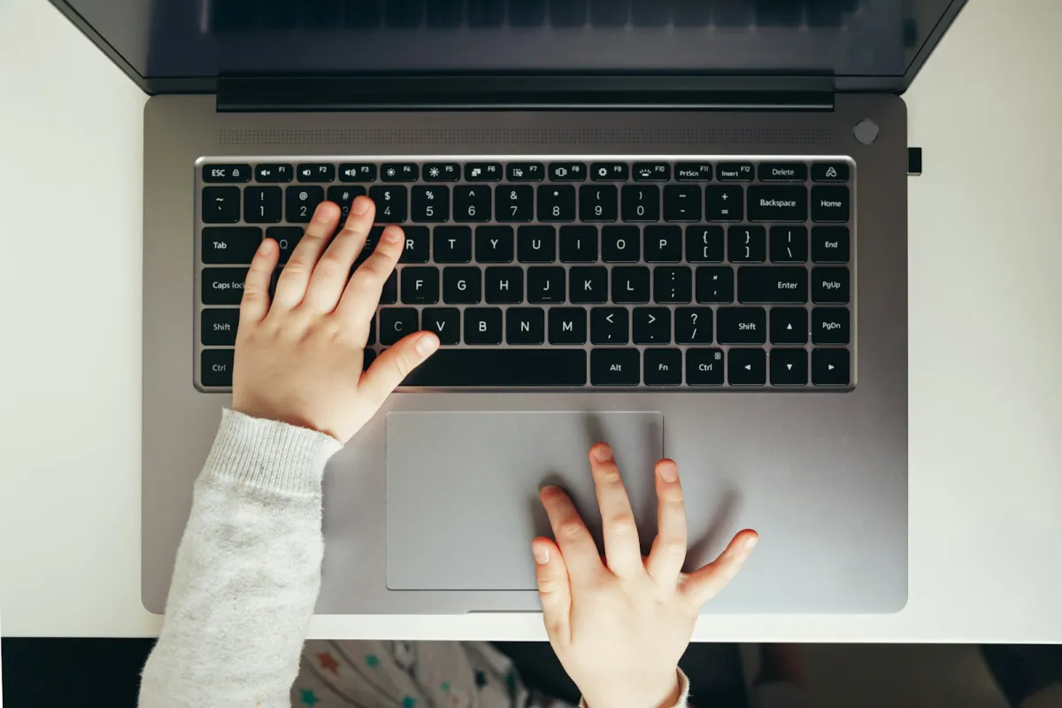A child's hands on a laptop keyboard and trackpad A child's hands on a laptop keyboard and trackpad