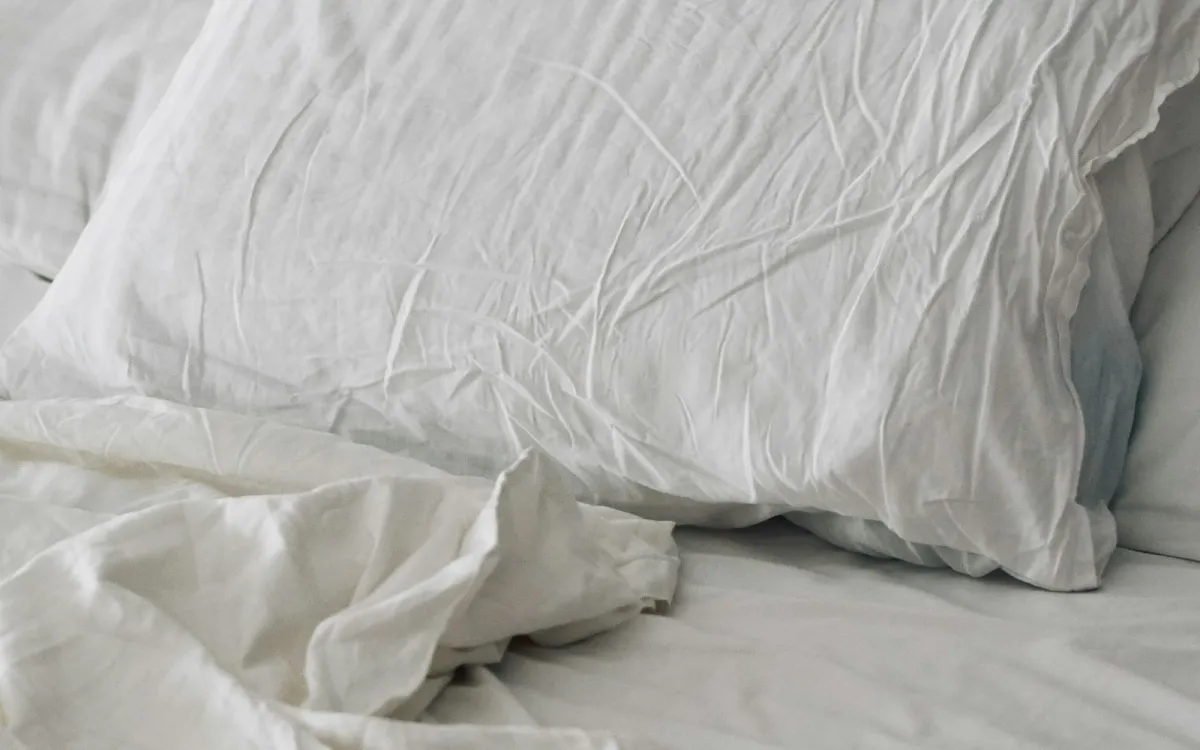 A rumpled white duvet and pillow on a bed in soft morning light A rumpled white duvet and pillow on a bed in soft morning light