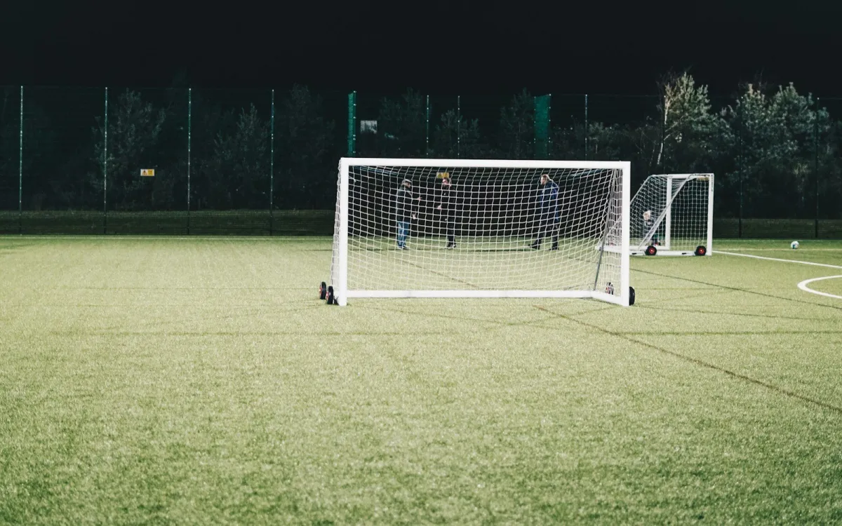 Floodlit grassroots football pitch at night with a portable goal