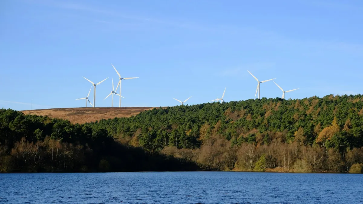 Wind turbines on a moorland ridge above woodland and a reservoir