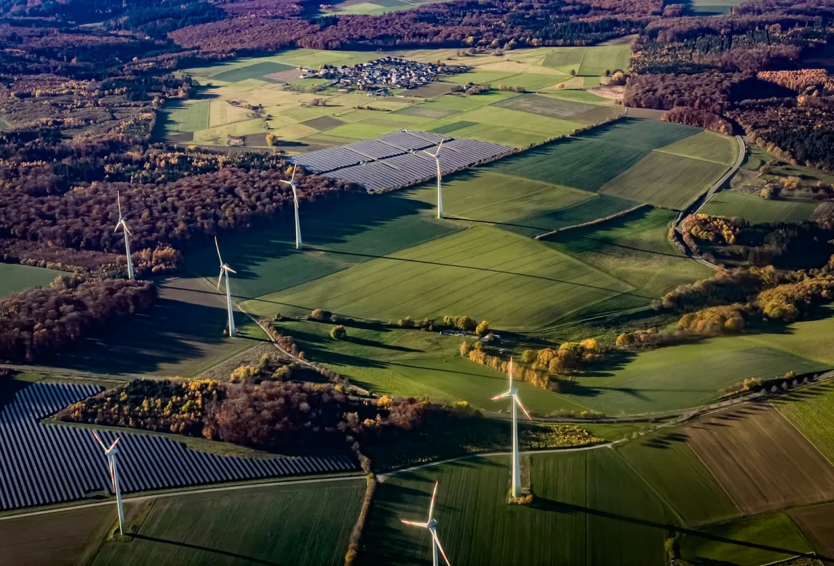Aerial view of wind turbines and solar farms among green fields and autumn woodland