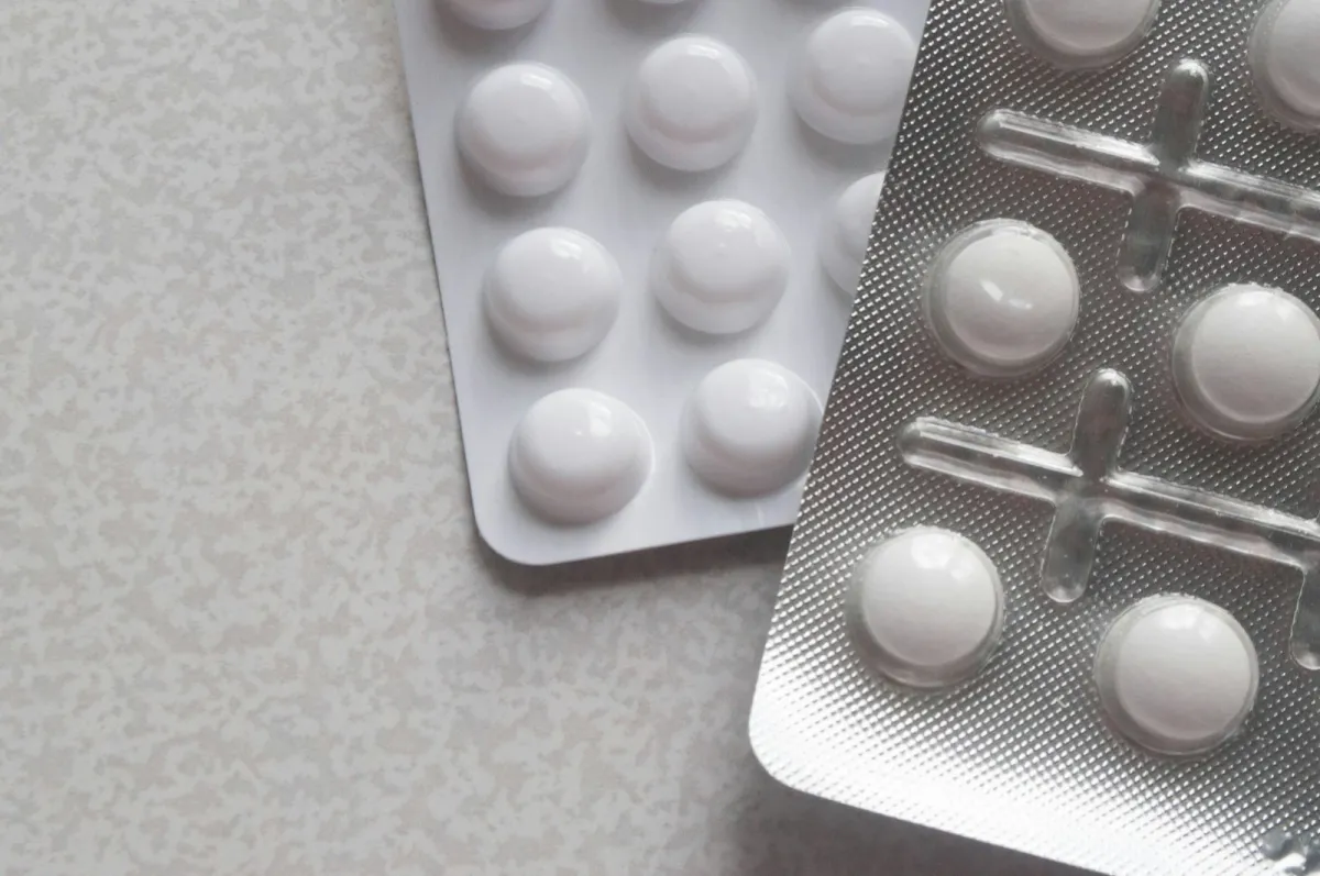 Two blister packs of white tablets on a pale speckled table Two blister packs of white tablets on a pale speckled table
