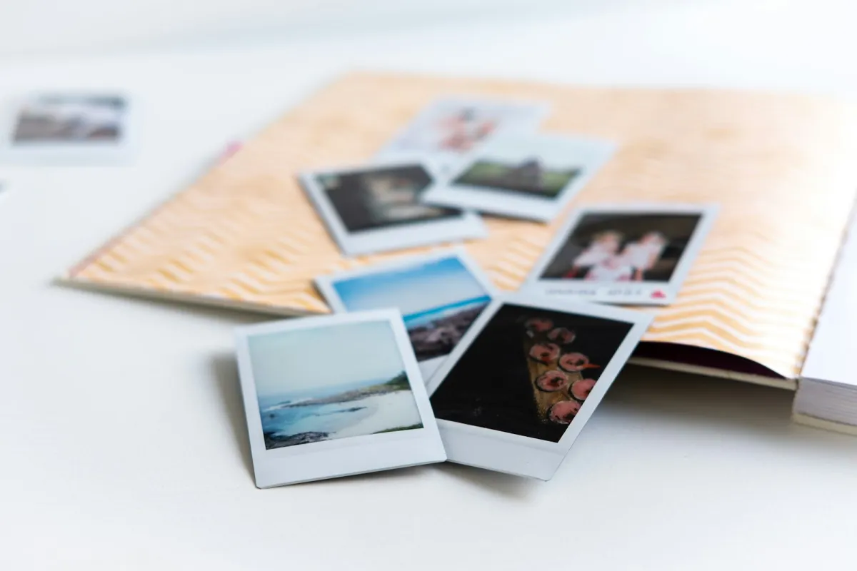 Instant photo prints spread over an open scrapbook on a white table Instant photo prints spread over an open scrapbook on a white table