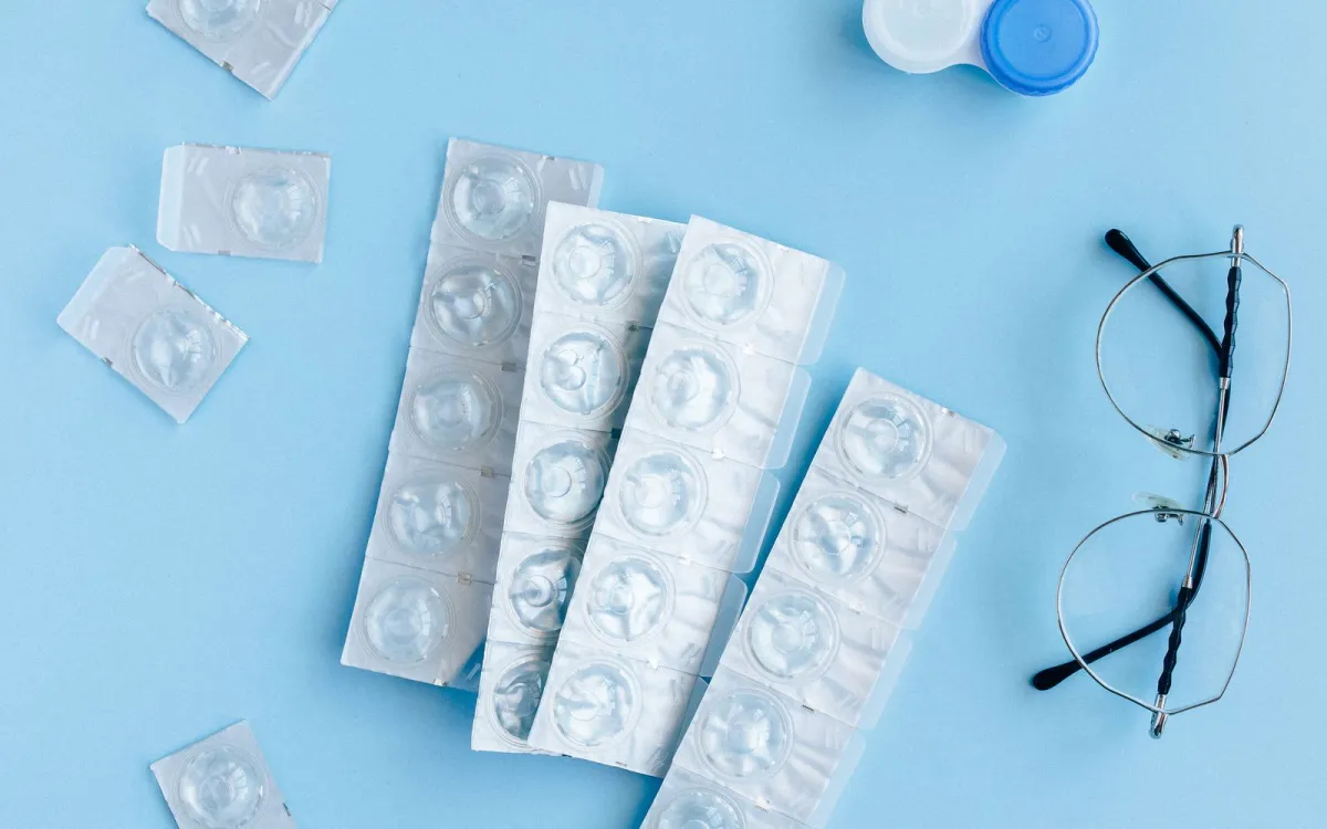 Blister packs of contact lenses, a lens case and a pair of glasses on a pale blue surface