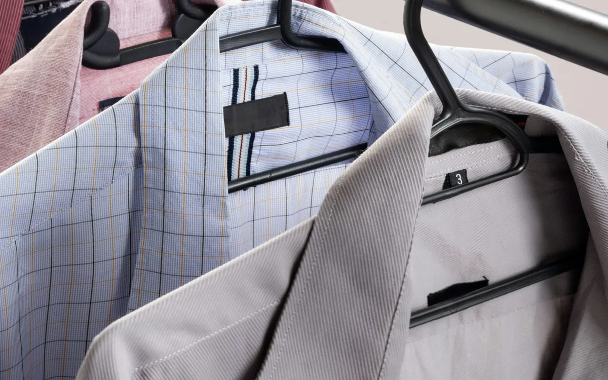 Men's shirts in pink, blue check and grey on black hangers on a clothes rail Men's shirts in pink, blue check and grey on black hangers on a clothes rail