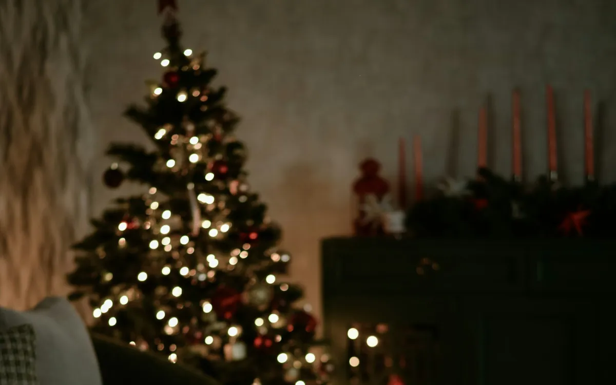 A lit Christmas tree in a dimly lit living room with candles on a sideboard A lit Christmas tree in a dimly lit living room with candles on a sideboard