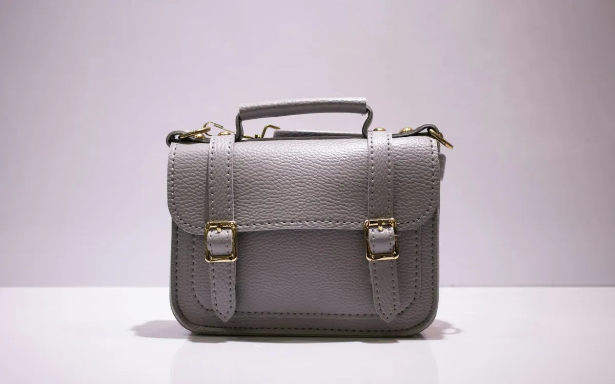 A grey leather satchel with gold buckles on a white surface