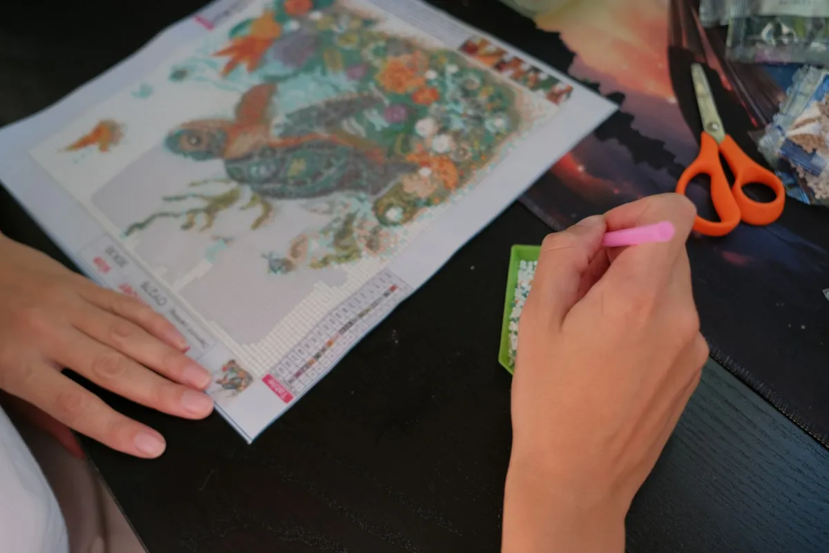 Hands placing gems on a sea turtle diamond painting at a table
