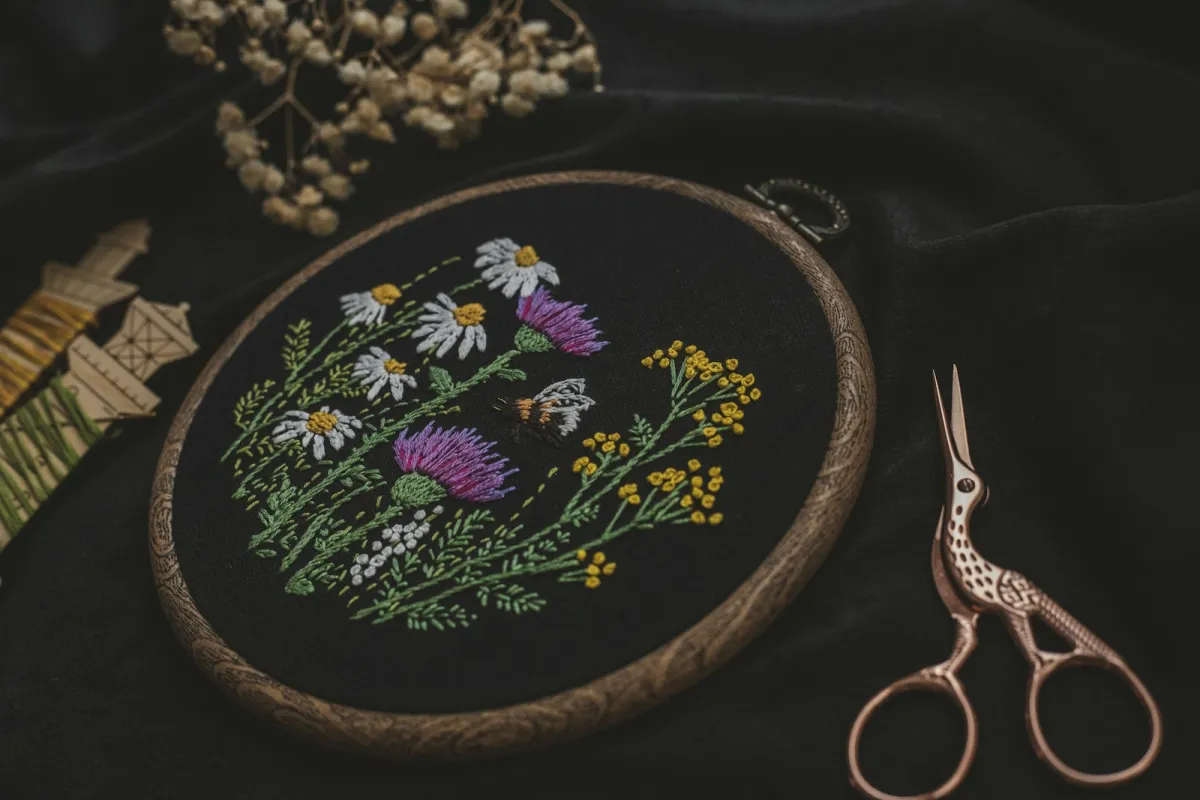 Wildflower embroidery in a wooden hoop beside thread and scissors Wildflower embroidery in a wooden hoop beside thread and scissors