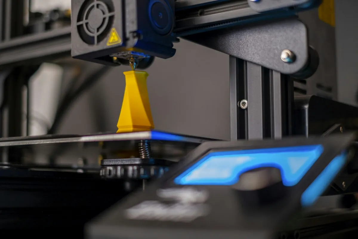 A 3D printer nozzle building a yellow plastic model on a lit print bed A 3D printer nozzle building a yellow plastic model on a lit print bed