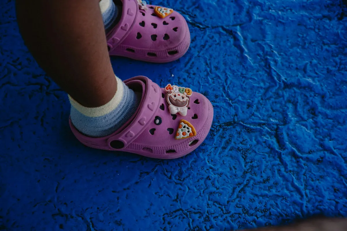 A child's feet in pink clogs decorated with charms on a blue mat A child's feet in pink clogs decorated with charms on a blue mat