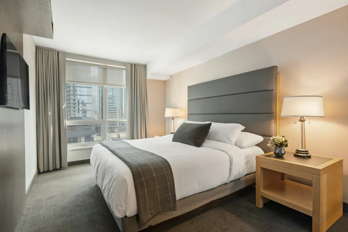 A made double bed with white duvet, pillows and a grey throw in a softly lit bedroom A made double bed with white duvet, pillows and a grey throw in a softly lit bedroom