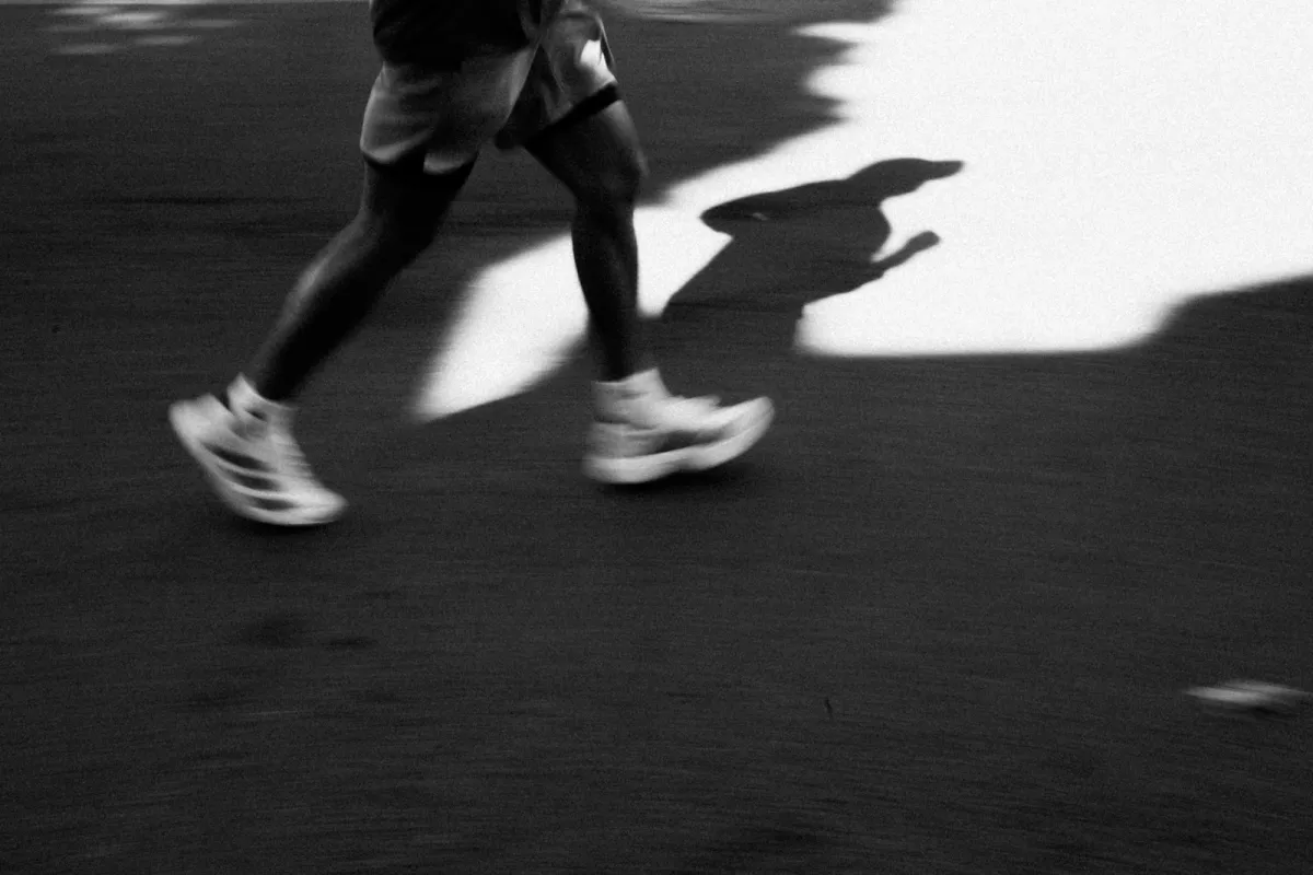 Black and white shot of a runner's legs and trainers in motion with a long shadow on the road