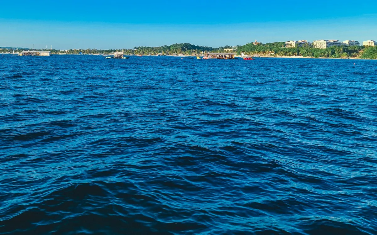 Deep blue sea off Boracay Island with boats and a palm-lined shore in the distance