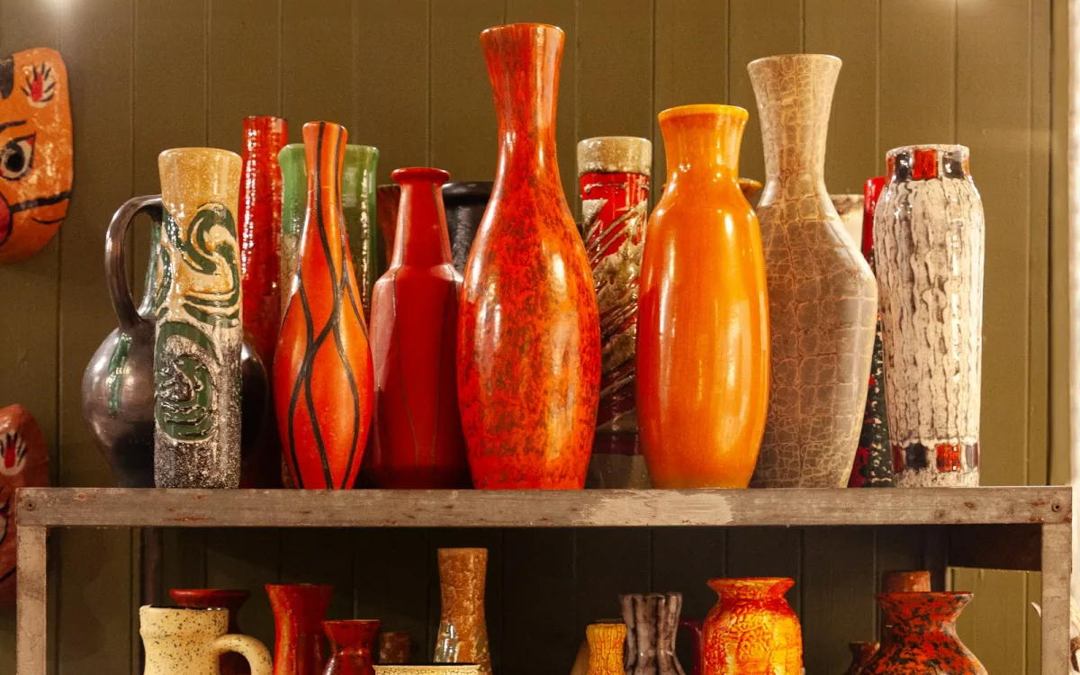 A shelf of colourful glazed vases in orange, red, green and cream against a dark panelled wall