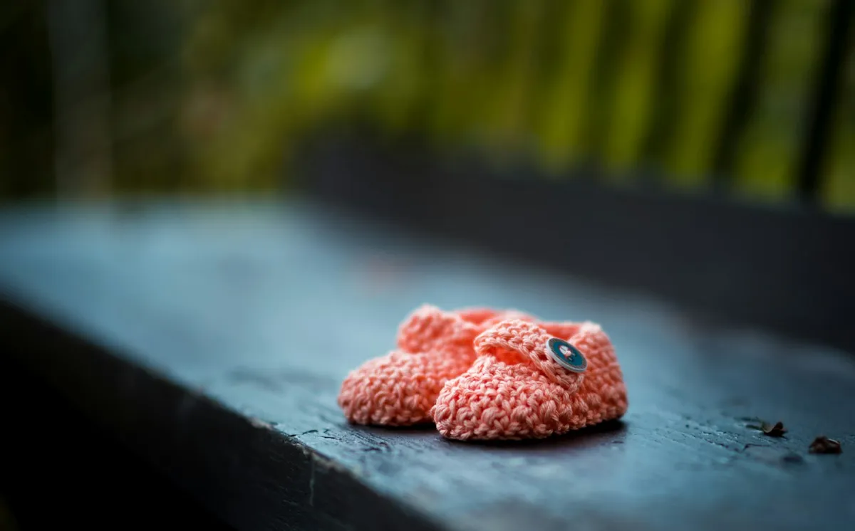 A pair of pink knitted baby shoes on a wooden bench