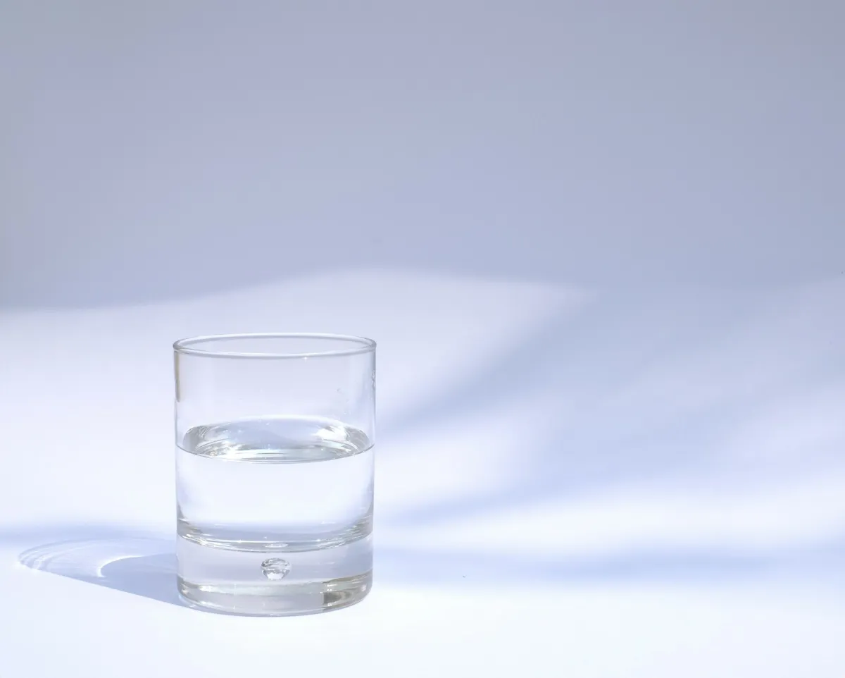 A clear glass half filled with water on a white surface in soft light