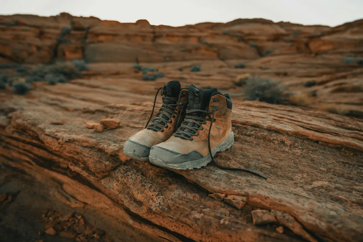 A pair of worn brown leather hiking boots standing on red sandstone rock