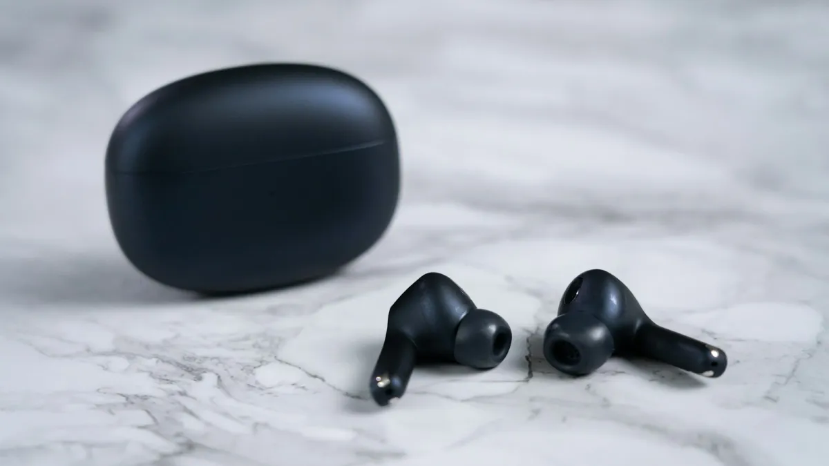A pair of black wireless earbuds beside their charging case on a marble surface