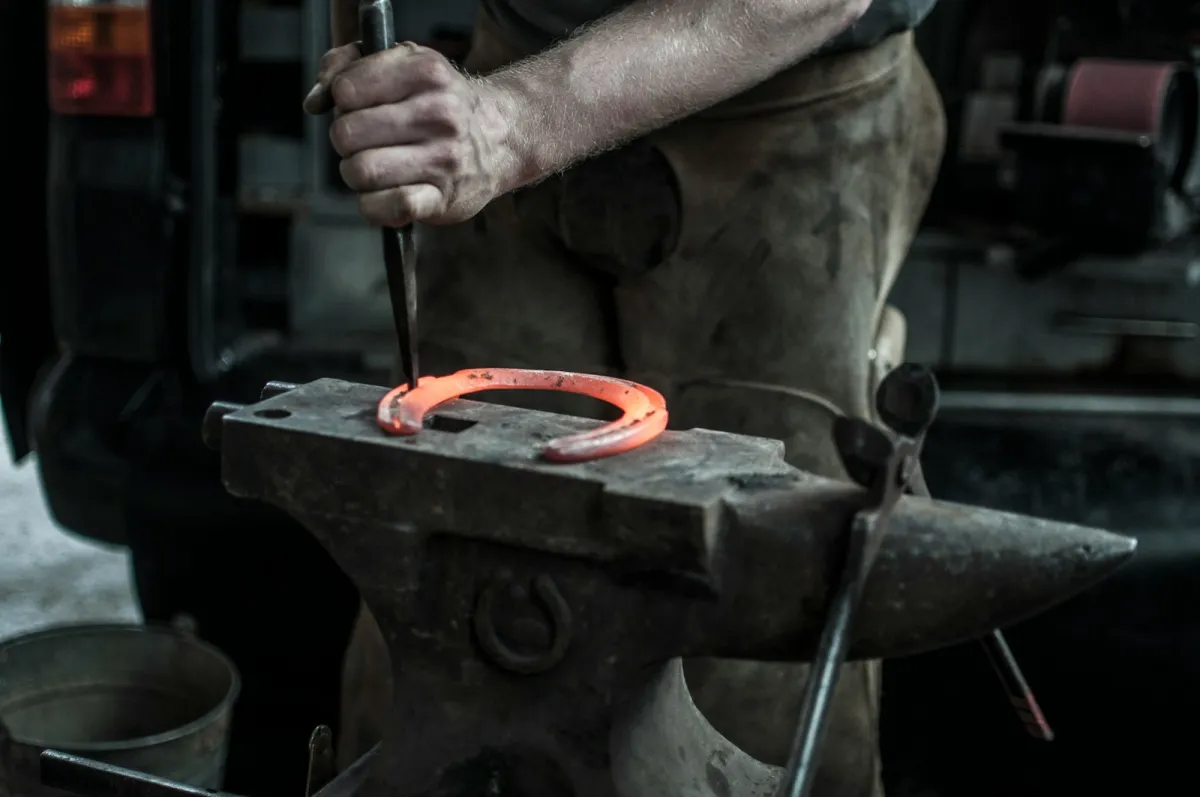 A horseshoe glowing orange on an anvil as a smith works it with a tool