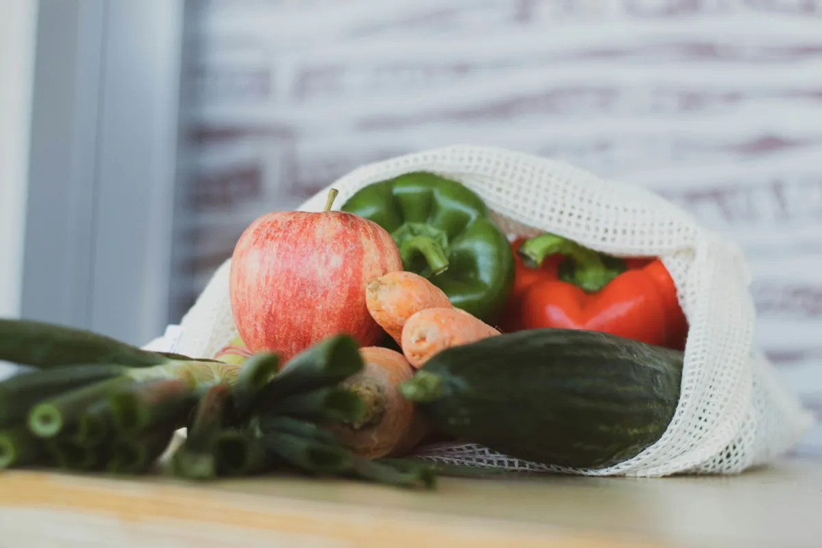 Fresh vegetables and an apple spilling out of a reusable cotton mesh produce bag Fresh vegetables and an apple spilling out of a reusable cotton mesh produce bag