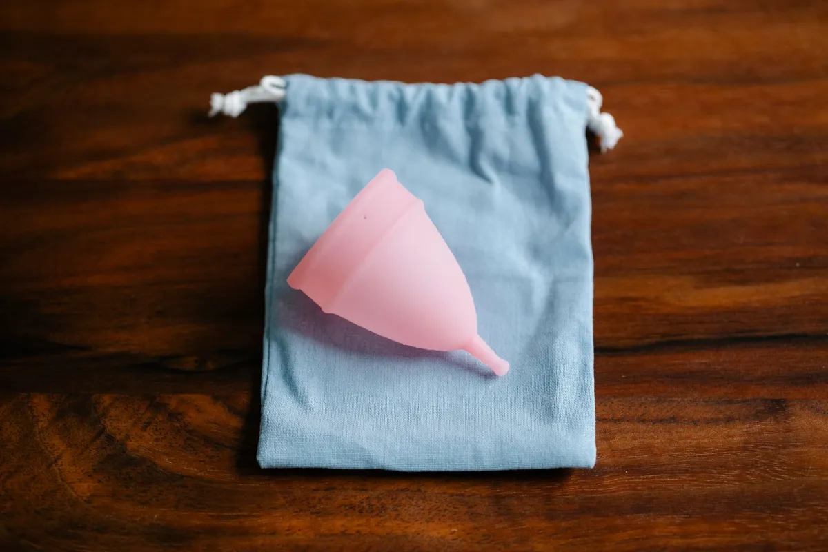 Pink silicone period cup resting on a blue cotton drawstring bag on a wooden table