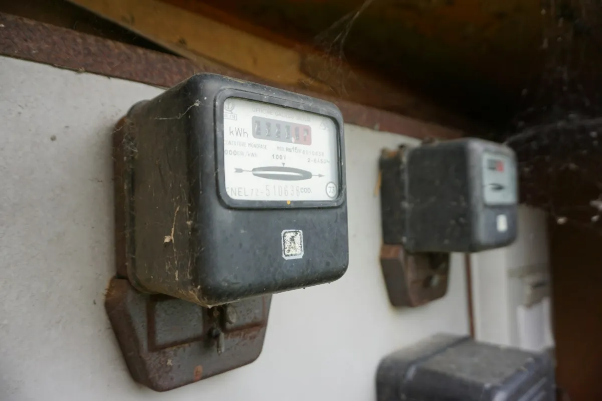 Two old black electricity meters with kWh dials mounted on a wall Two old black electricity meters with kWh dials mounted on a wall