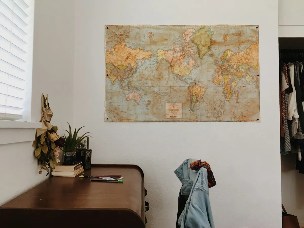 A vintage-style world map pinned to a white wall above a wooden desk with a plant and books