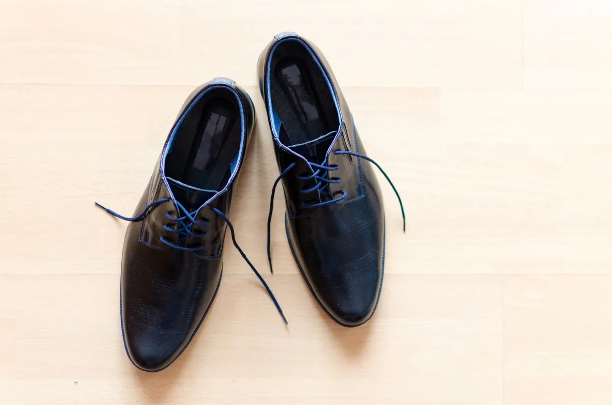 A pair of black leather lace-up shoes with blue laces on a pale wooden floor A pair of black leather lace-up shoes with blue laces on a pale wooden floor
