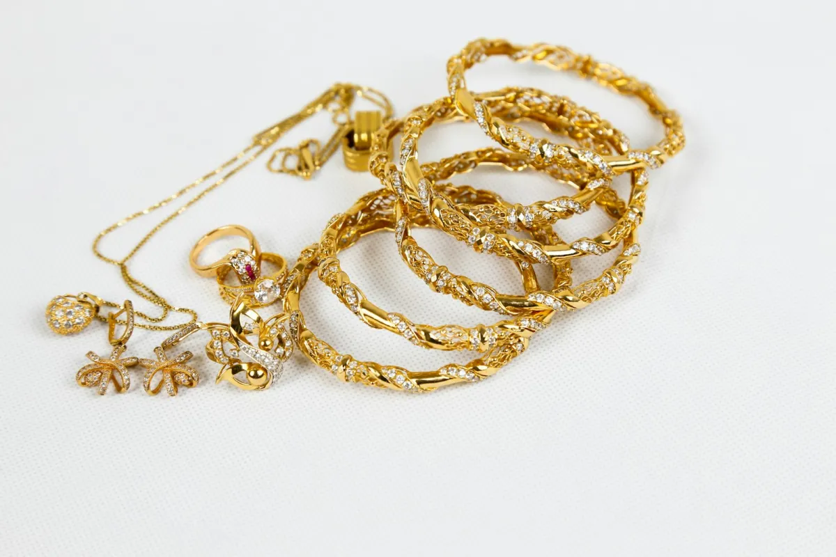 Gold bangles, rings, earrings and a fine chain necklace on a white surface