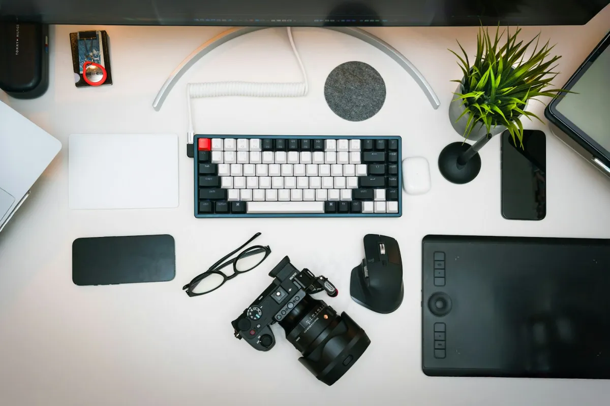 A tidy white desk seen from above with a keyboard, camera, mouse, glasses and a drawing tablet A tidy white desk seen from above with a keyboard, camera, mouse, glasses and a drawing tablet