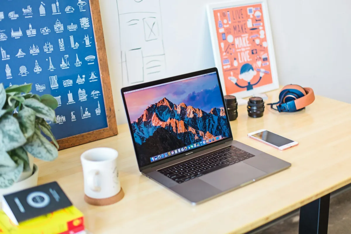 Open laptop on a wooden desk beside a mug, phone, headphones and framed prints Open laptop on a wooden desk beside a mug, phone, headphones and framed prints
