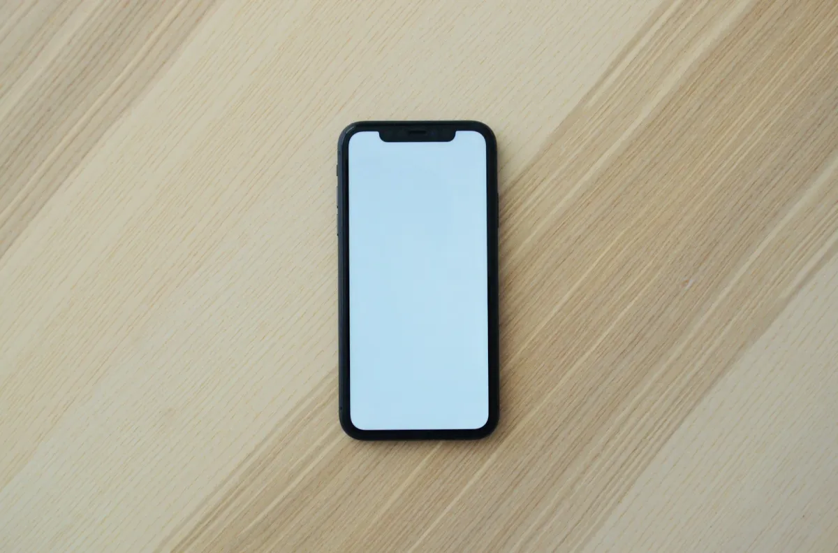 A black smartphone with a blank screen lying on a light wooden table