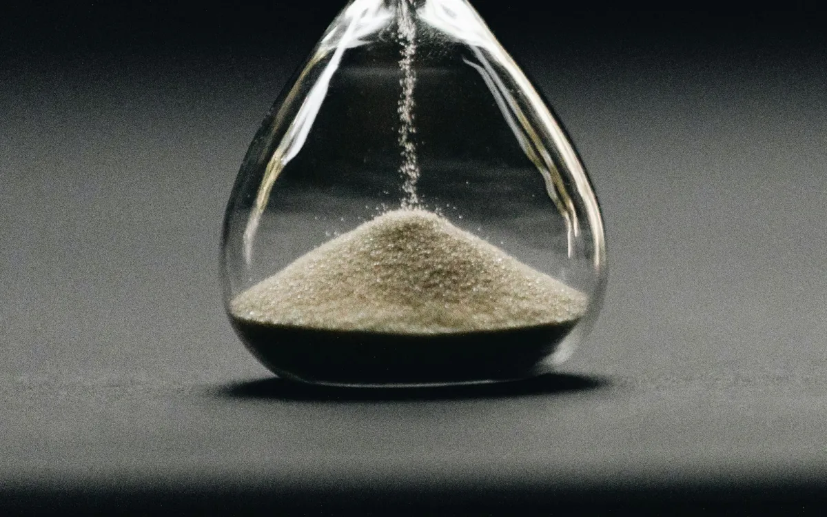 Sand running through a glass hourglass against a dark grey background Sand running through a glass hourglass against a dark grey background