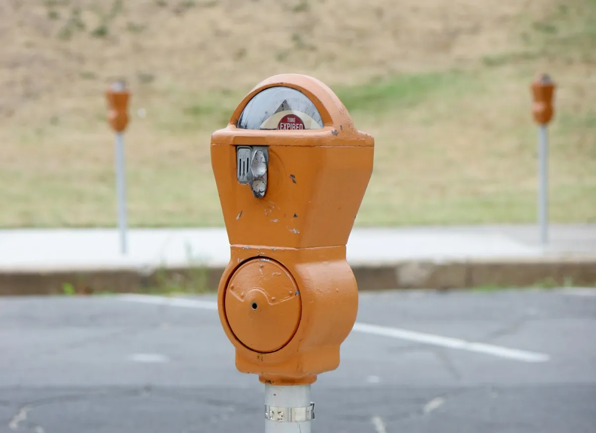 An orange coin parking meter beside an empty car park, with more meters in the background An orange coin parking meter beside an empty car park, with more meters in the background