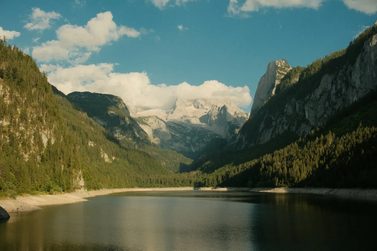 A calm Alpine lake below forested slopes and snowy peaks at Gosauseen, Austria A calm Alpine lake below forested slopes and snowy peaks at Gosauseen, Austria