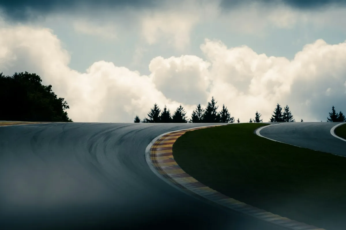 An empty curving race track with red and yellow kerbs under a cloudy sky