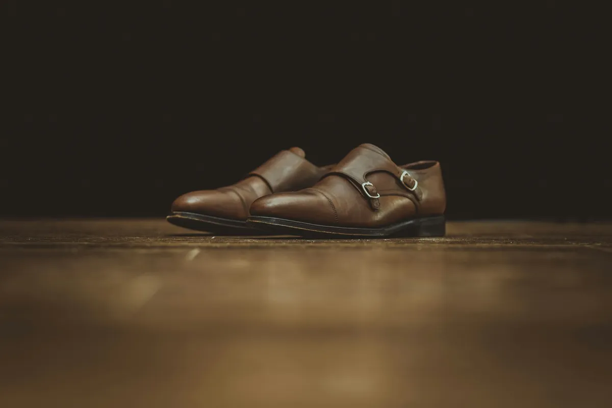 A pair of brown leather double monk strap shoes on a wooden floor A pair of brown leather double monk strap shoes on a wooden floor