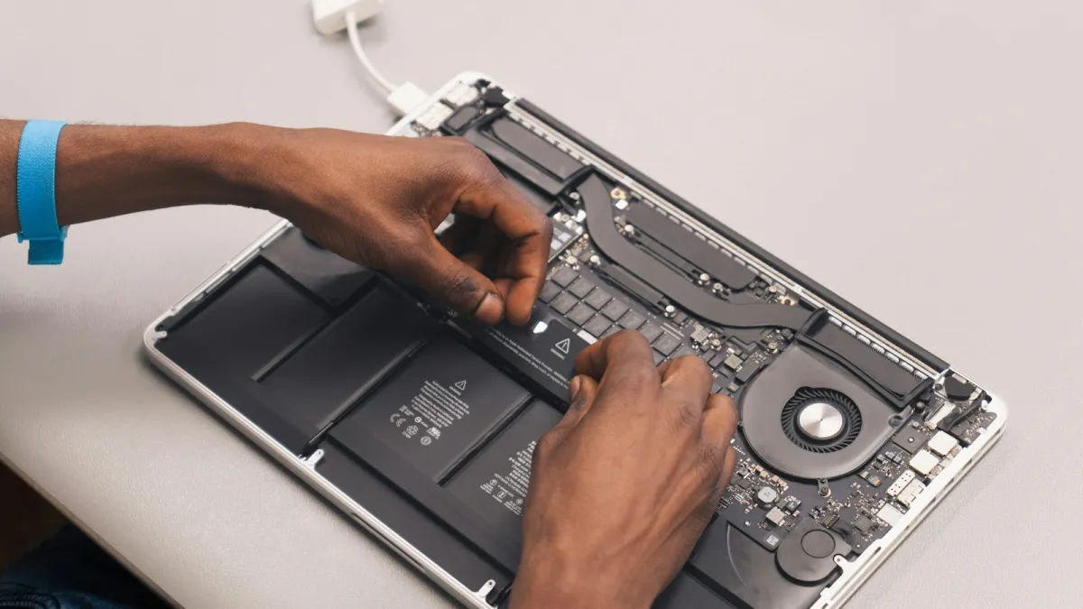 Hands working inside an opened laptop with the bottom panel removed, showing the battery, fan and circuit board Hands working inside an opened laptop with the bottom panel removed, showing the battery, fan and circuit board