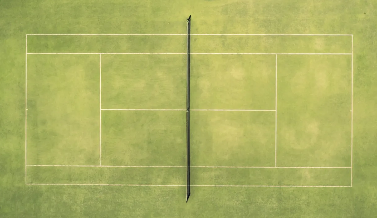 Overhead view of a green grass tennis court with white lines and a net Overhead view of a green grass tennis court with white lines and a net