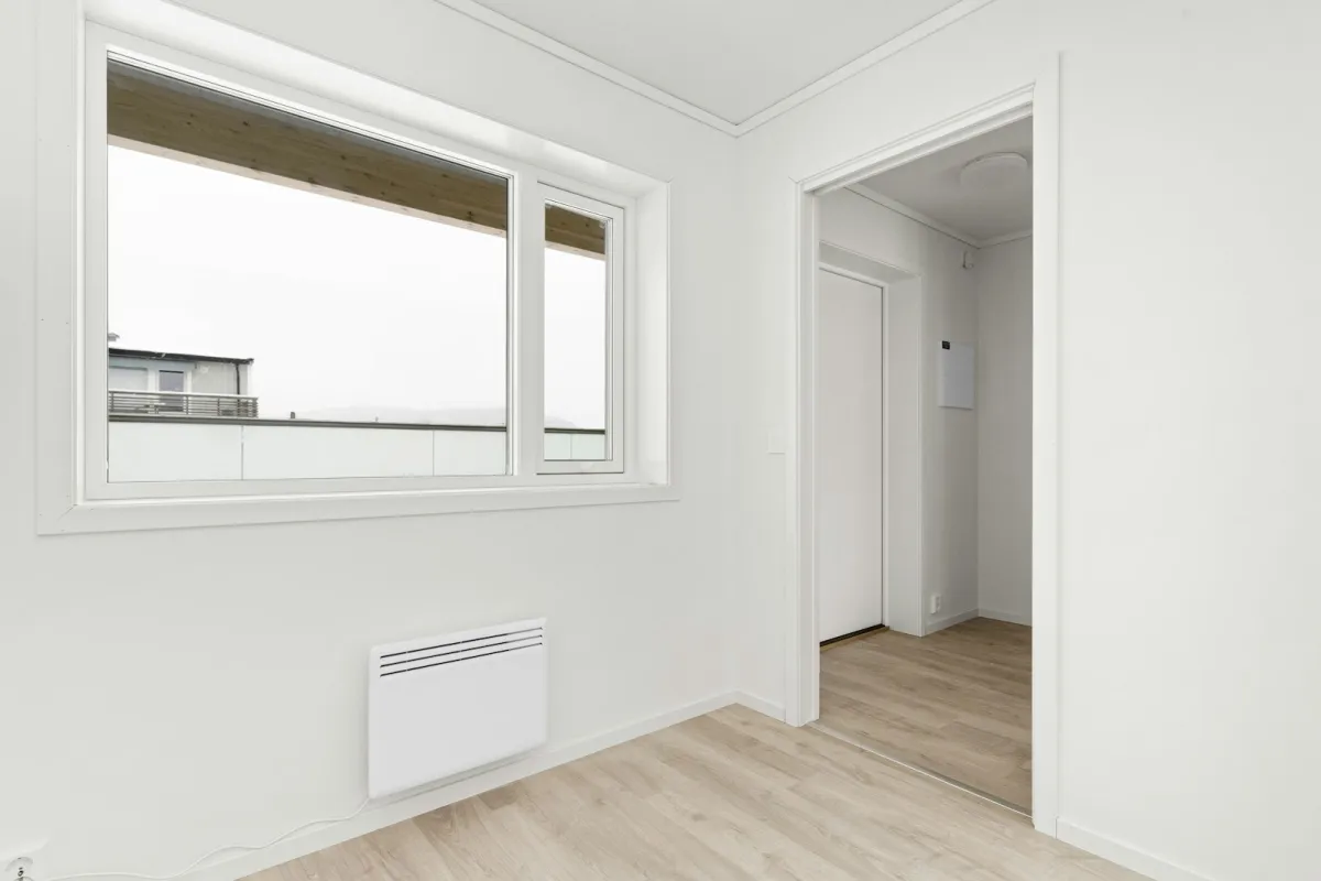 A bright, empty room with a white panel heater on the wall beneath a window A bright, empty room with a white panel heater on the wall beneath a window