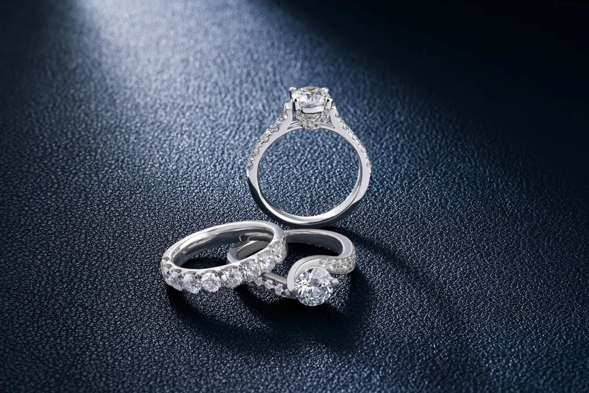 Three silver diamond rings on a dark textured surface under a soft spotlight